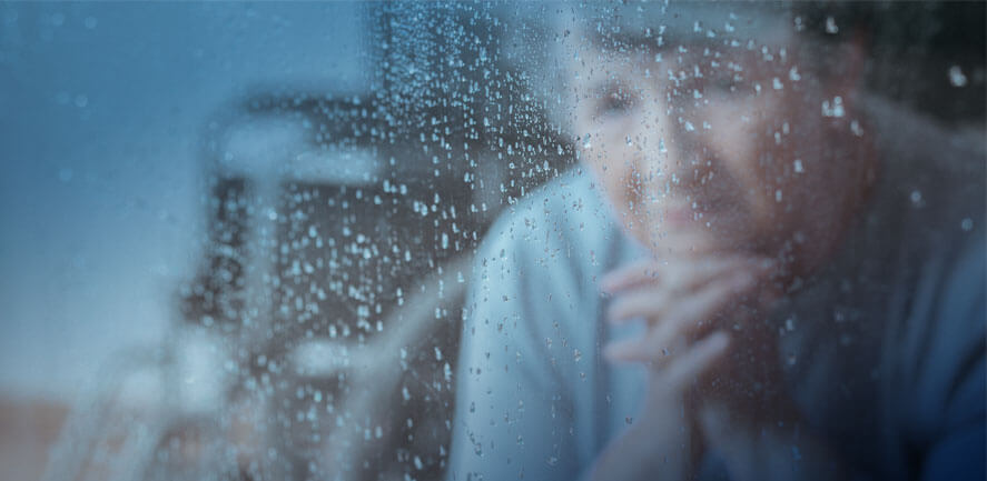 Elderly woman with gray hair looking through a rain covered window 